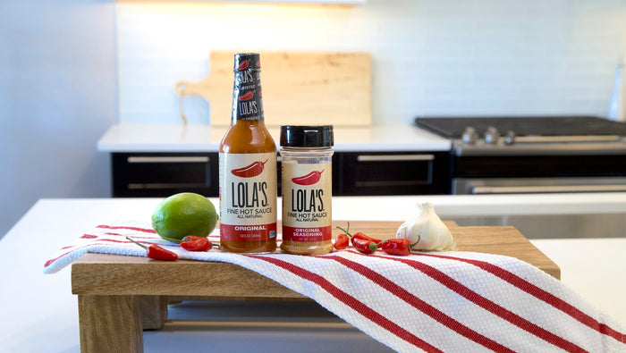 A collection of hot sauce bottles, lime, and chili peppers from Lola's Fine Sauces.