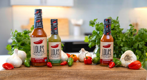Bottles of hot sauces and vegetables on a table from Lola's Fine Sauces collection.
