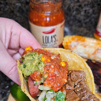 A hand holding Lola's Smoked Bacon & Sweet Corn Salsa, a delicious fusion of premium Iowa bacon & Midwest sweet corn in homemade salsa.