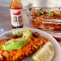 A plate of food with a lime wedge and Lola's Ghost Pepper Hot Sauce bottle.