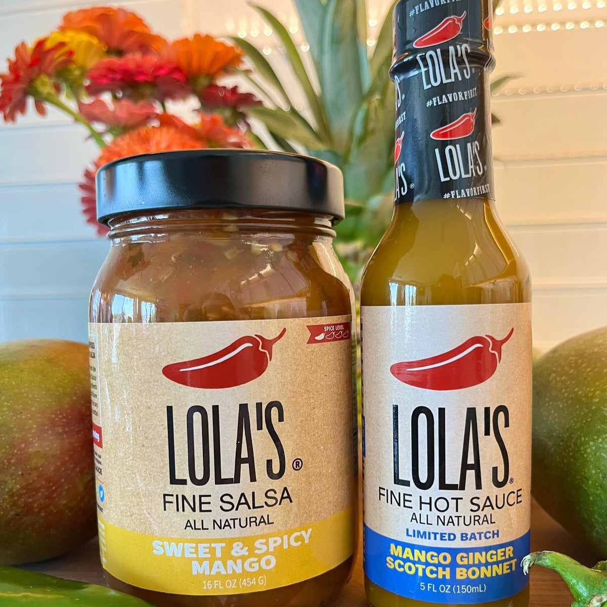 Lola's Mango Ginger Scotch Bonnet Hot Sauce, a couple of jars of hot sauce and a jar of salsa on a table, a bottle of hot sauce, a close up of a green vegetable and a green pepper on a wooden surface.