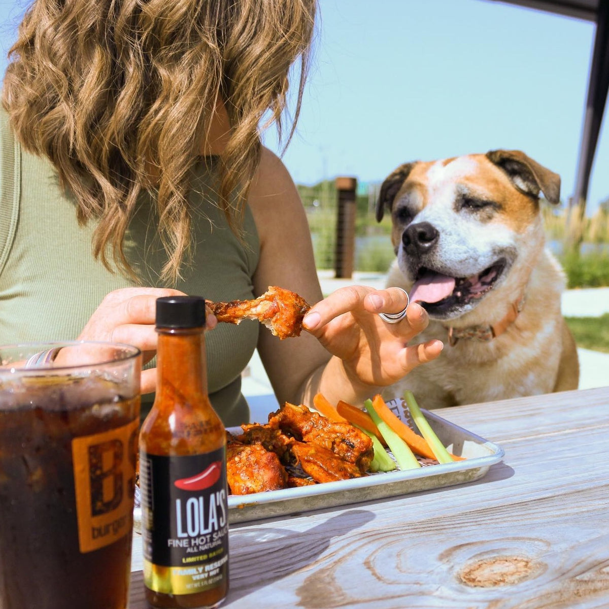 A woman with a dog enjoying Lola's Family Reserve Hot Sauce, a spicy blend of Carolina reaper and habanero peppers. 5 oz. glass bottle with gift box.