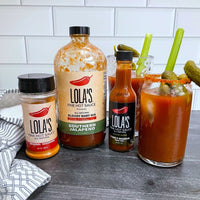 Lola's "Game Day" Bundle: Bottles of hot sauce, a glass of liquid, and a jar of sauce on display.