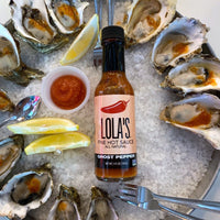 A plate of oysters with Lola's Ghost Pepper Hot Sauce, lemon, and a bottle of sauce.