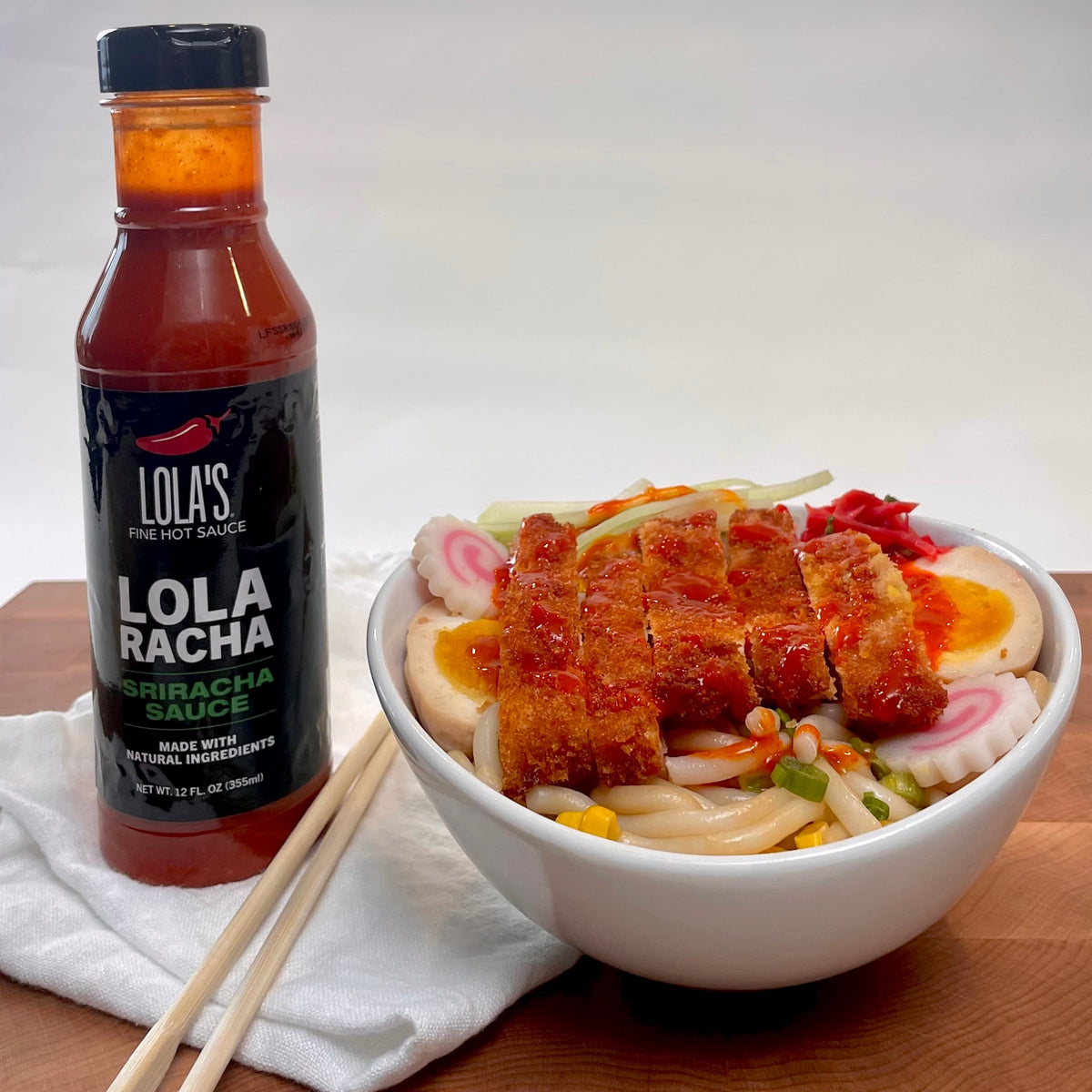 A bowl of food with Lola's Sriracha sauce and chopsticks, perfect for adding a spicy kick to any dish.