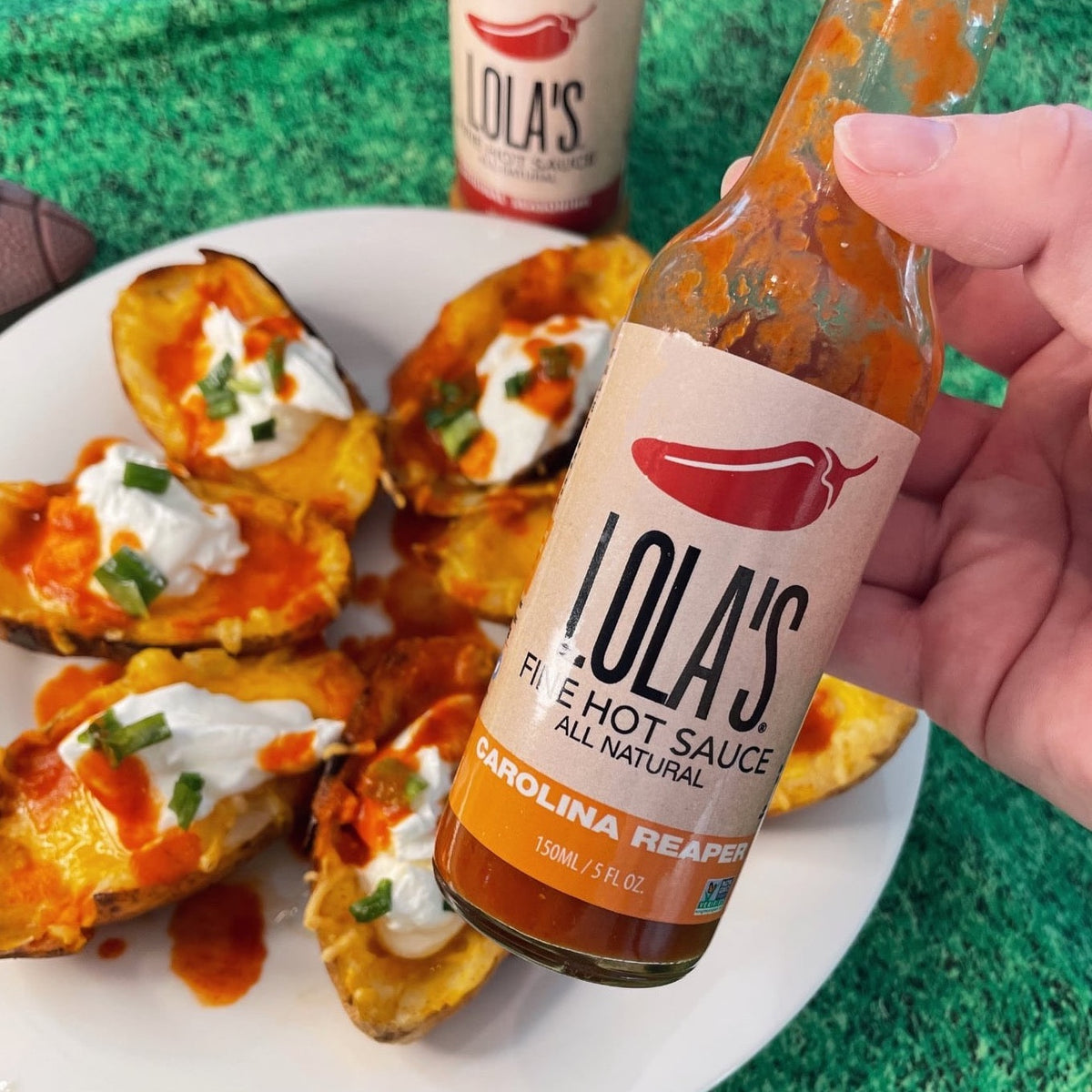 A hand holding Lola's Carolina Reaper Hot Sauce bottle, perfect for pizza, meal prep, or pasta! 5 oz. glass bottle. All-natural, plant-based, keto, low sodium, non-GMO, and gluten-free.